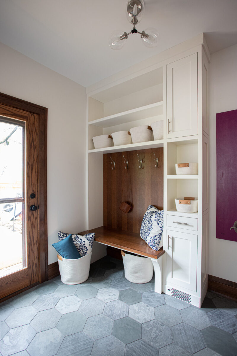 Twin Cities mudroom renovation features white built-ins, wood bench, and hexagonal grey tile floor.