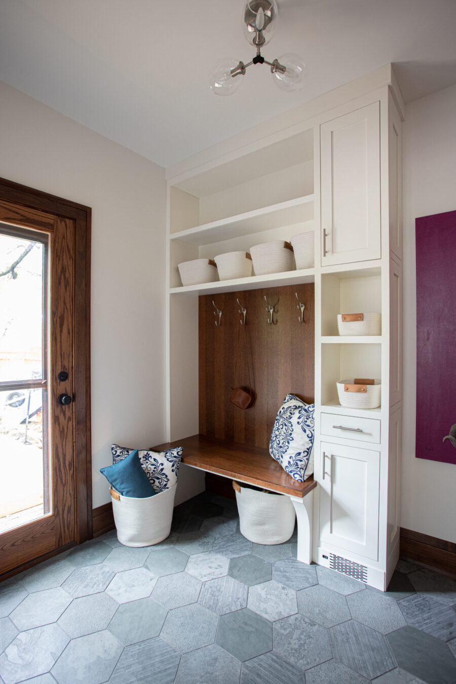 Twin Cities mudroom renovation features white built-ins, wood bench, and hexagonal grey tile floor.