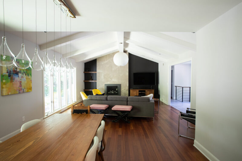 Contemporary home renovation features vaulted white ceilings, dark wood floors, and a stone fireplace.