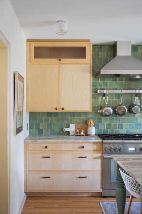 A bright kitchen remodel features light wood cabinetry, a green tile backsplash, and modern stainless steel appliances.