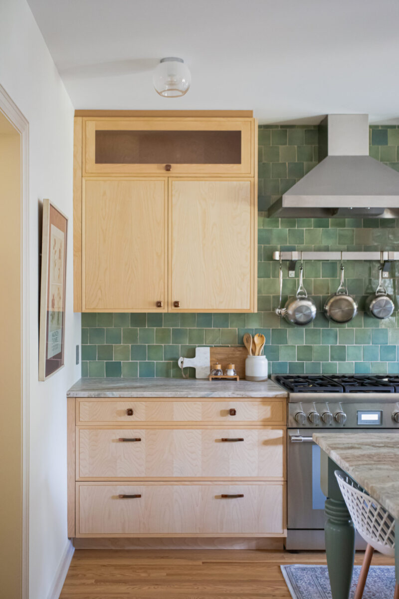 A bright kitchen remodel features light wood cabinetry, a green tile backsplash, and modern stainless steel appliances.