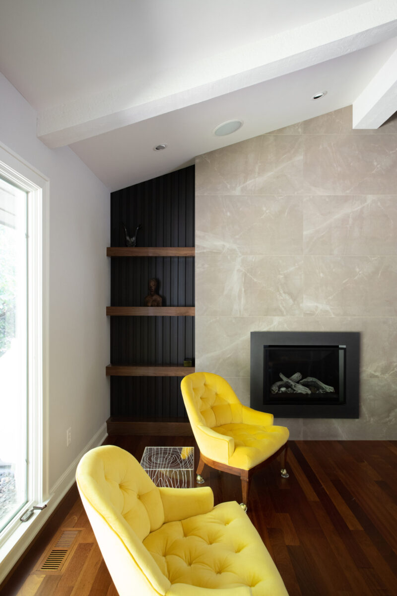 Twin Cities design-build: marble fireplace, dark wood floors, bright yellow chairs, and black built-in shelves.