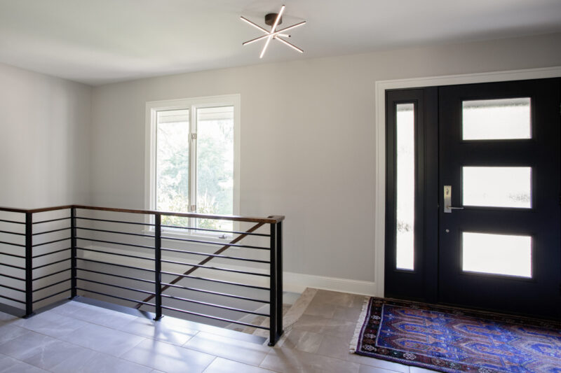 Twin Cities entryway renovation features black door, horizontal railing, and contemporary lighting.