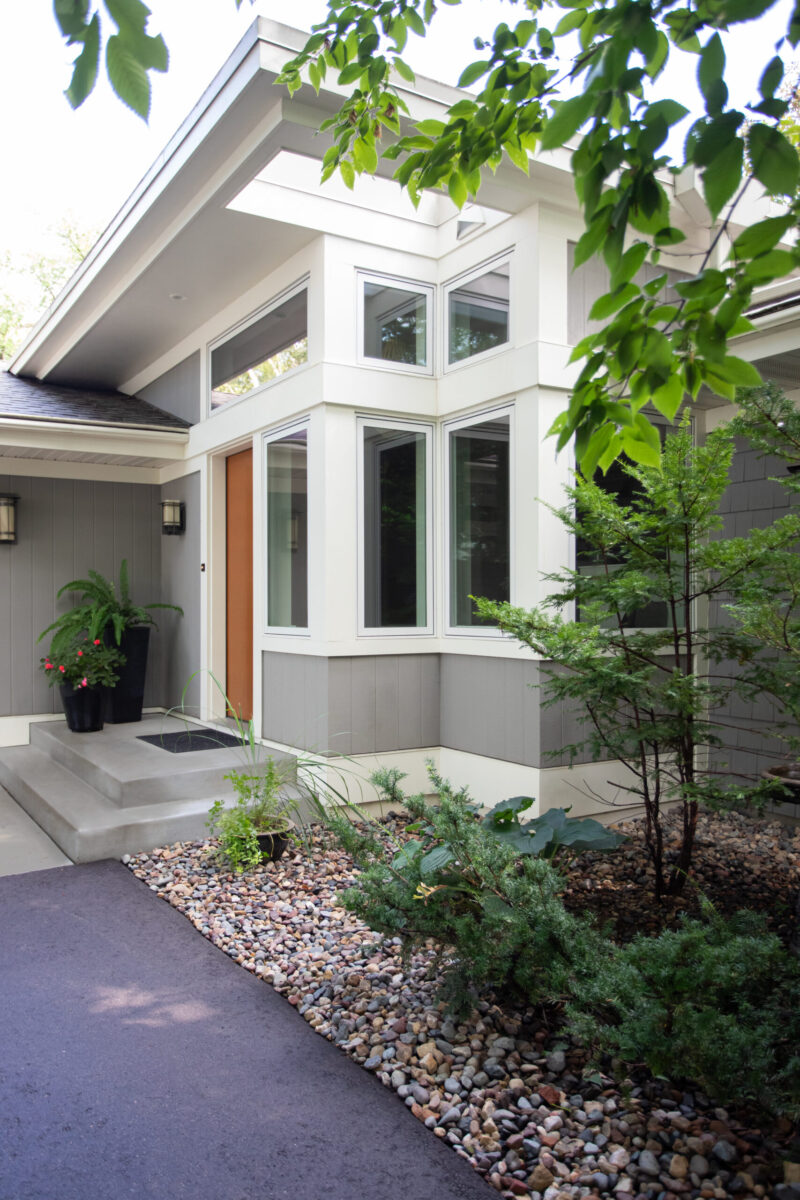 Contemporary residence features gray paneling, expansive corner windows, inviting landscaping.