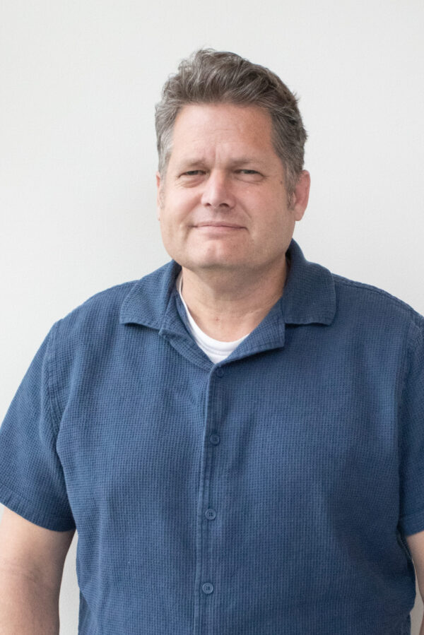 A grey-haired professional wears a distinct blue textured short-sleeve button-down shirt.
