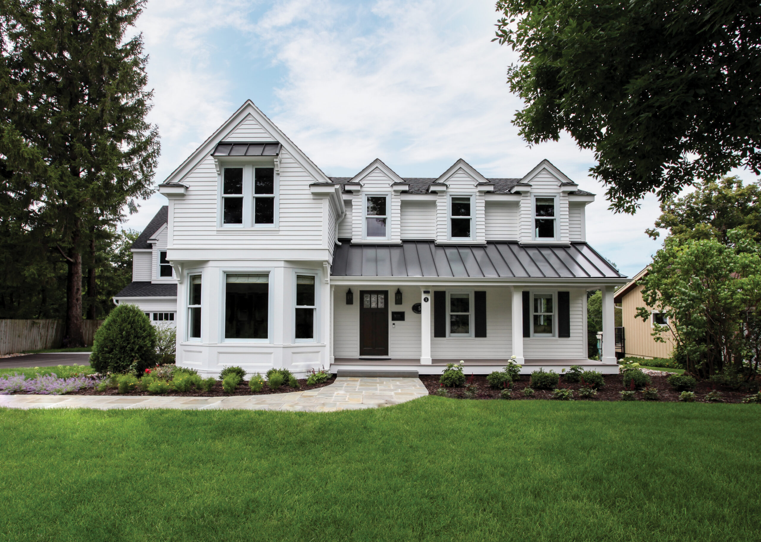 white two story home with dormers black metal porch roof and lush front lawn