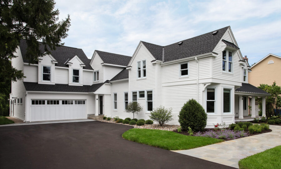 Expansive white clapboard house renovation features new black shingled roof, professional landscaping.