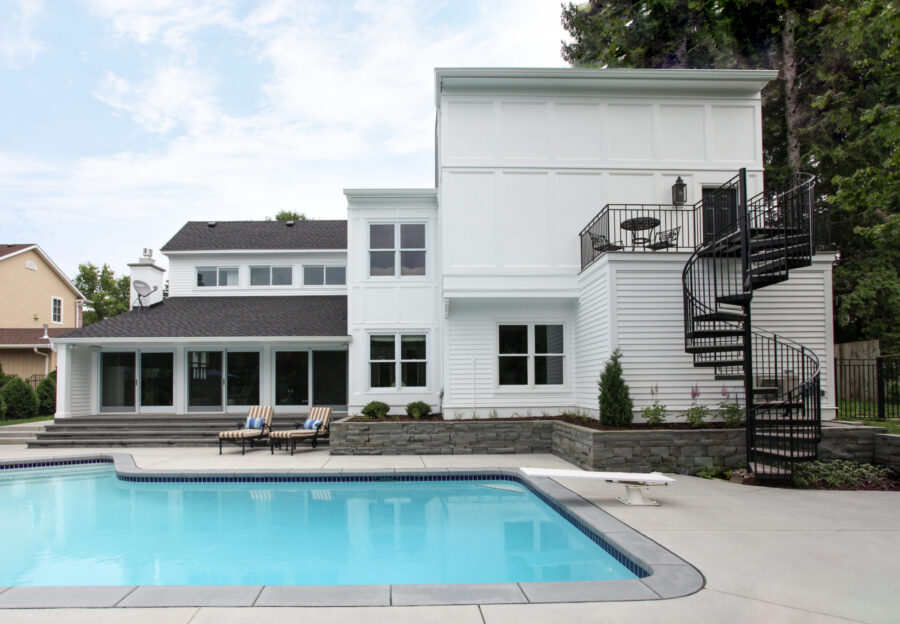 Contemporary white exterior remodel features expansive pool, black spiral staircase, stone walls.