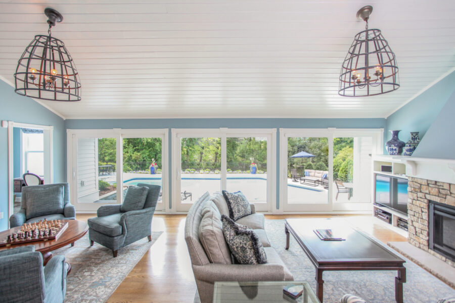 Renovated living room: vaulted plank-ceiling, stone fireplace, pool-facing doors.