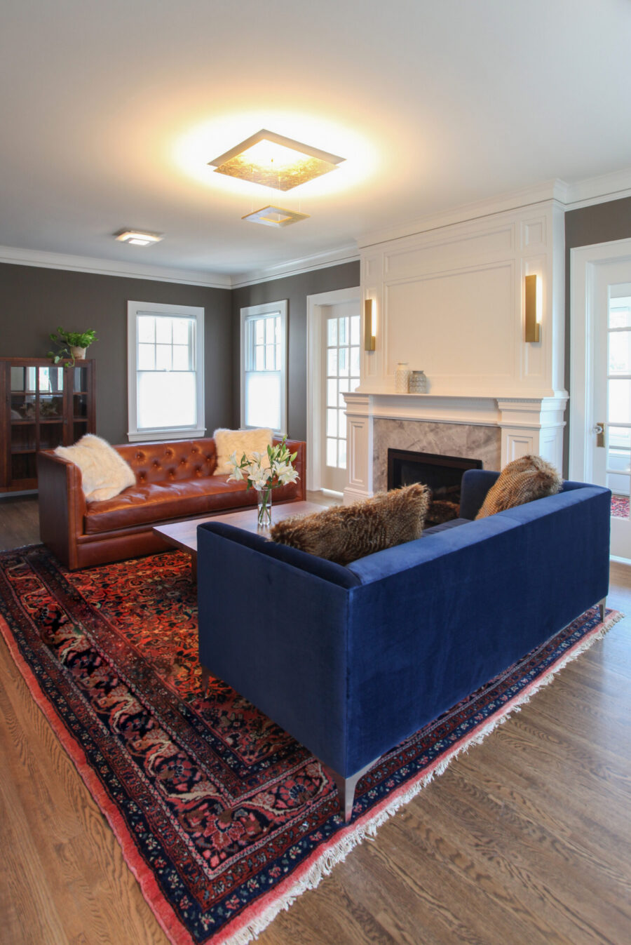 Twin Cities renovation: white fireplace, dark walls, wood floor, and plush blue and brown sofas.