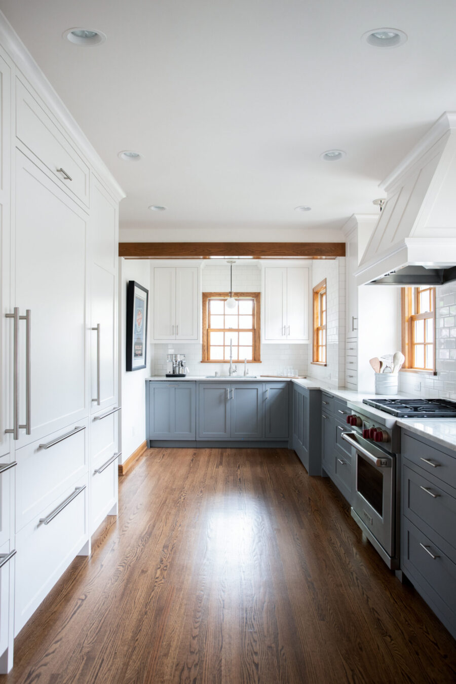 Modern galley kitchen remodel features two-tone cabinets, dark hardwood, ample lighting.