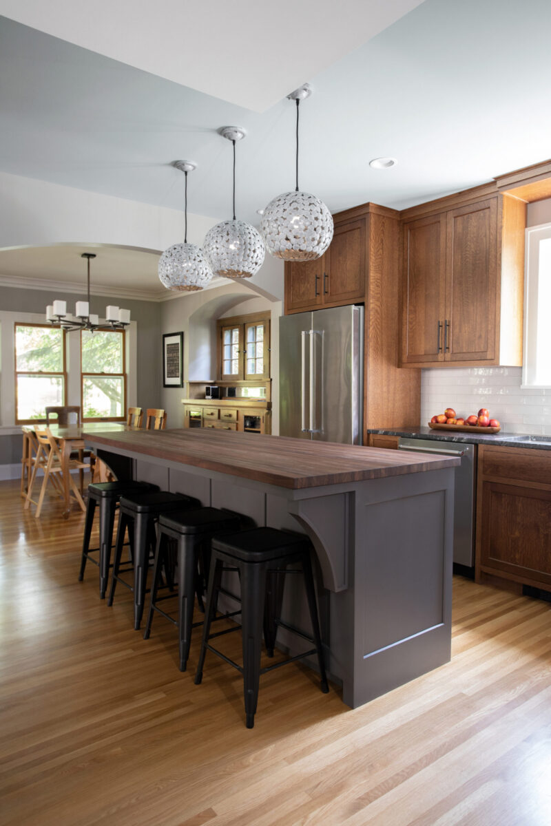 Kitchen remodel features gray island, wood-countertop, stylish pendants.