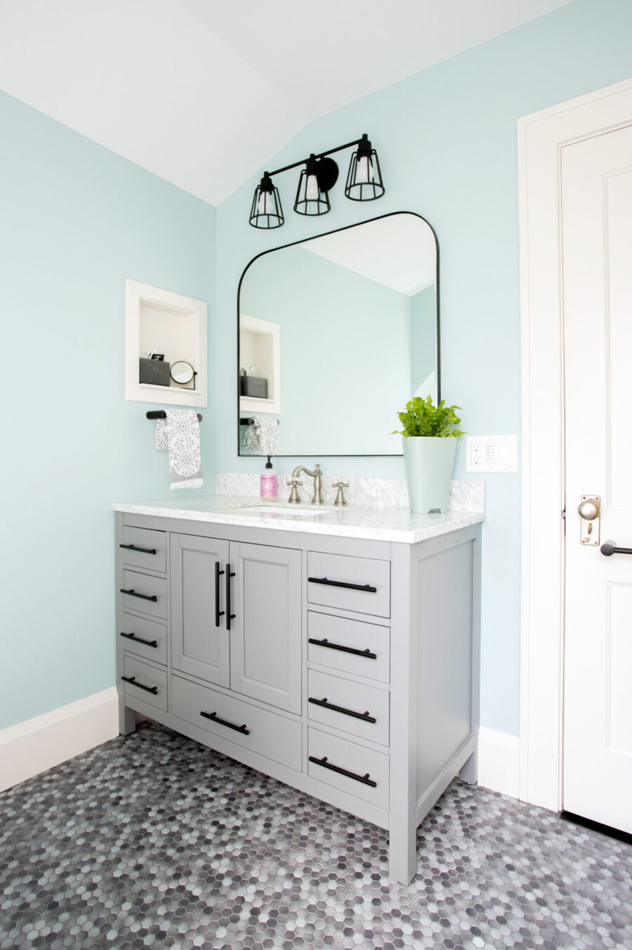 Aquamarine bathroom renovation: gray cabinetry, hexagonal flooring, black accents.