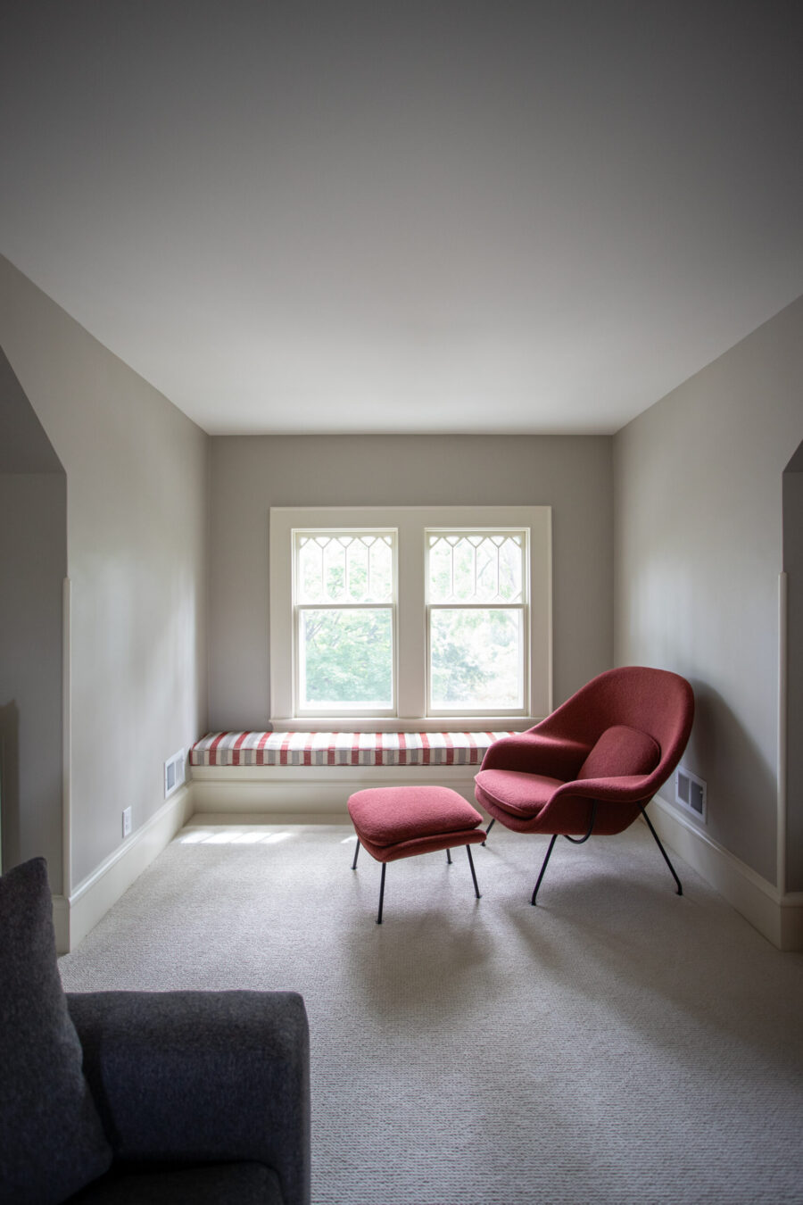 Upper-level sitting area with custom window bench, neutral carpet, and modern lounge chair