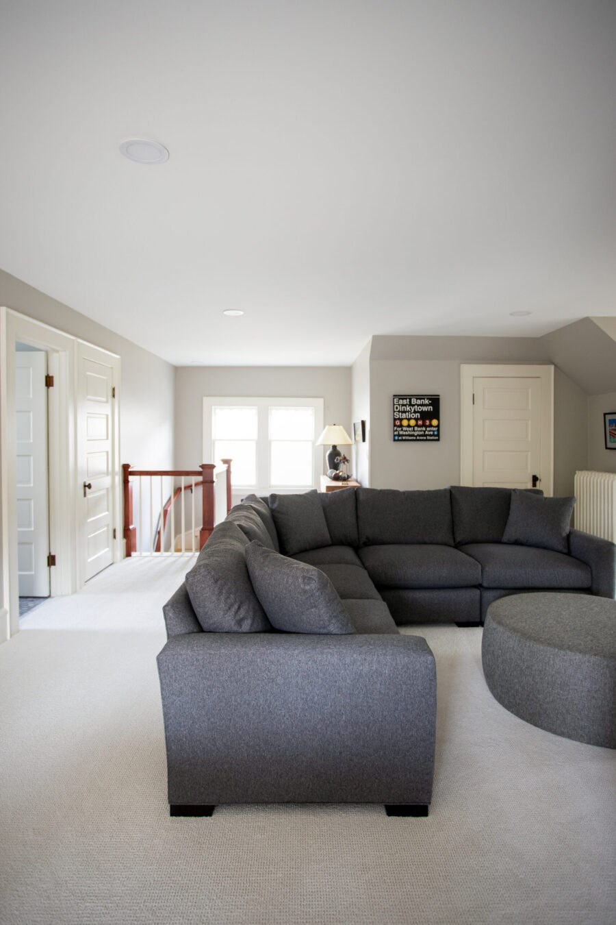 Finished attic living space with sectional sofa, stair railing, and natural light from windows