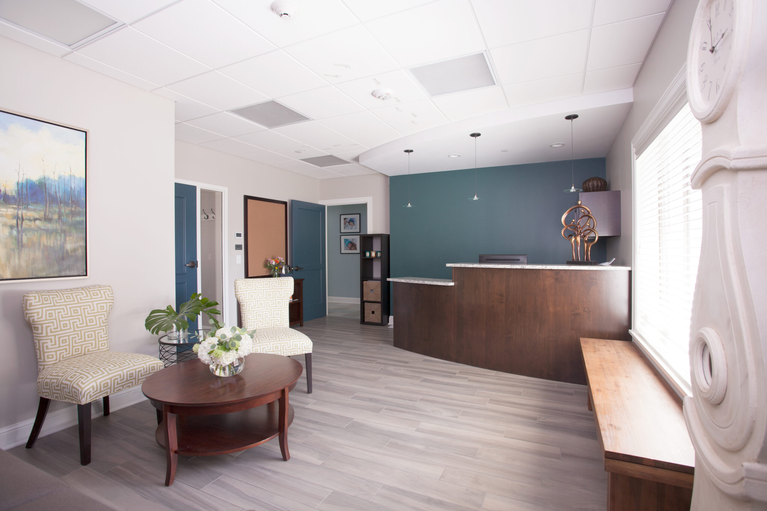 Modern office reception area with teal accent wall, dark wood desk, seating area, and architectural interior design elements.