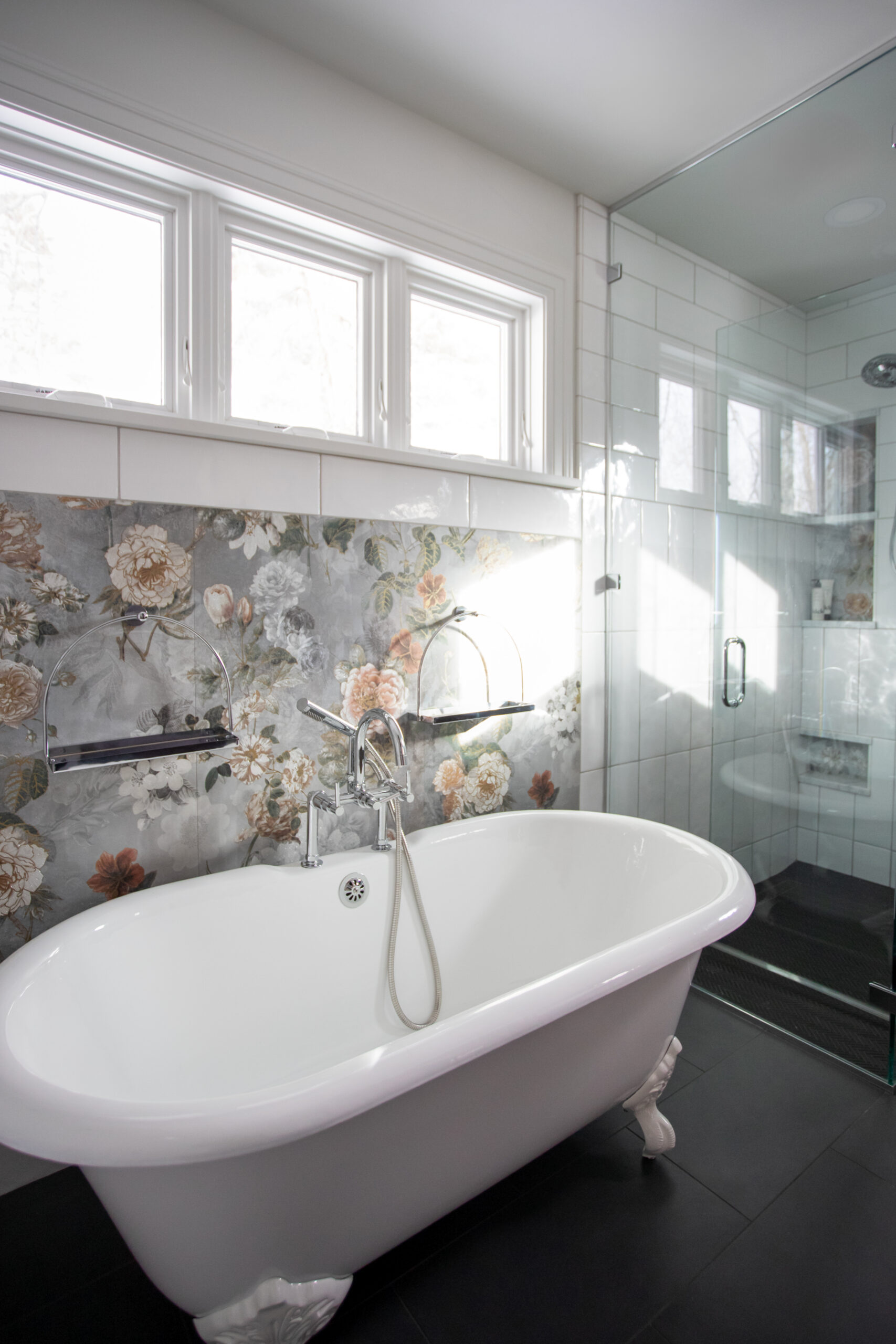 Luxury bathroom with freestanding white bathtub, floral tile backsplash, glass shower enclosure, and bright windows
