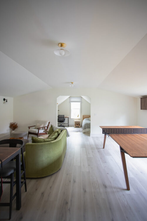 Open-concept loft space with vaulted ceilings, green curved chair, wooden dining table, and architectural design services creating seamless flow between rooms.