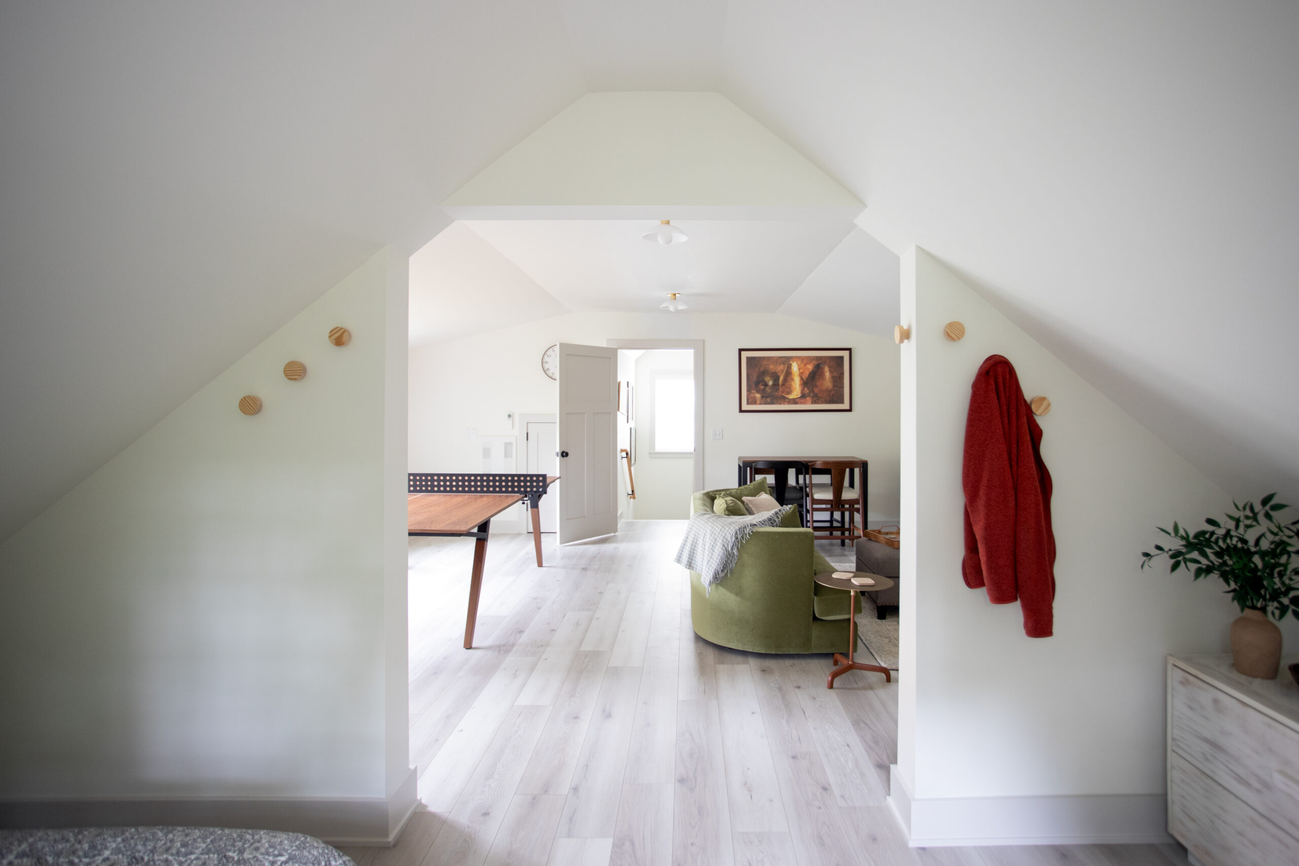 Bright attic bedroom with sloped ceilings, light wood flooring, and open floor plan leading to living area with green sofa and architectural design elements.