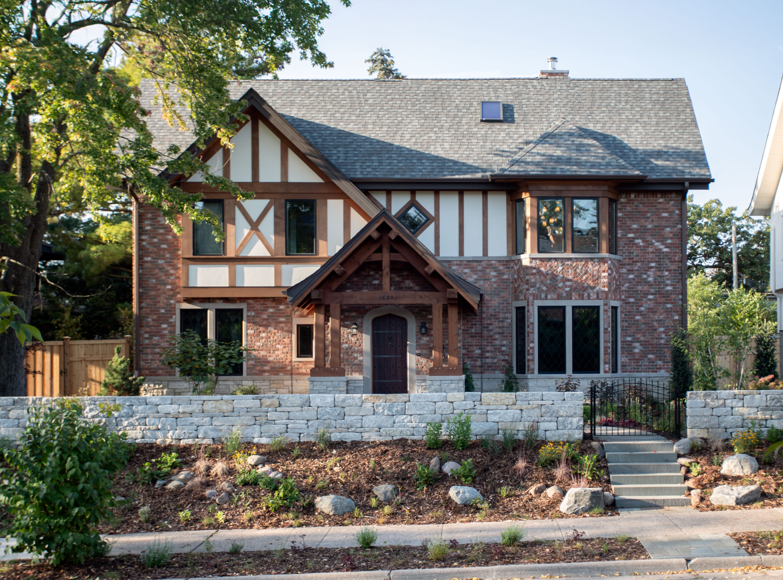 Tudor-style brick house with cream and dark timber framing, stone foundation, and manicured landscaping