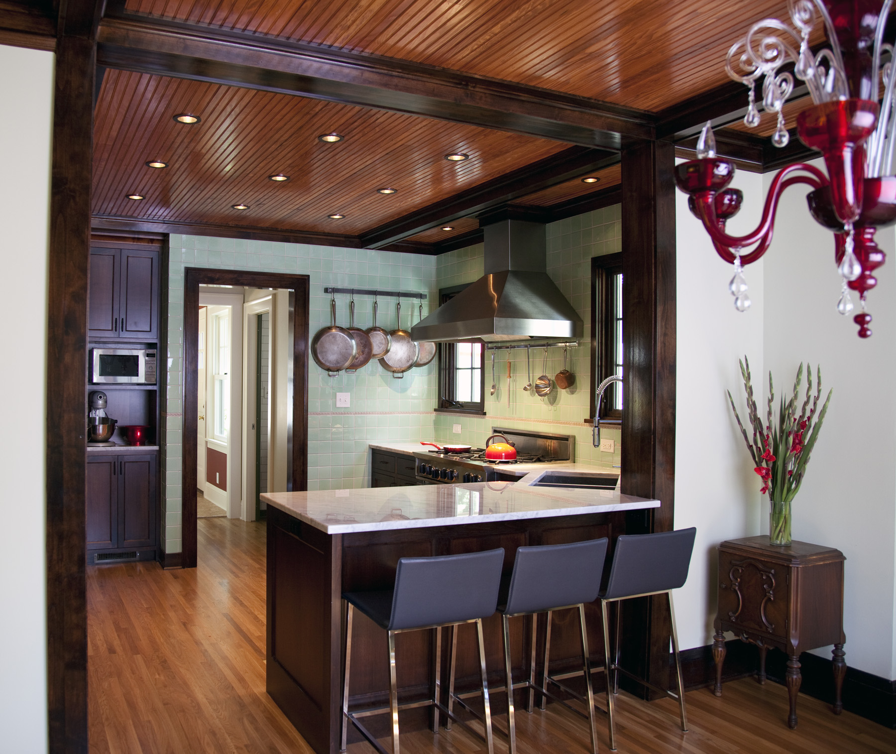 Modern kitchen with wood ceiling, island seating, mint tile backsplash, and custom home additions featuring dark cabinetry and stainless steel appliances.