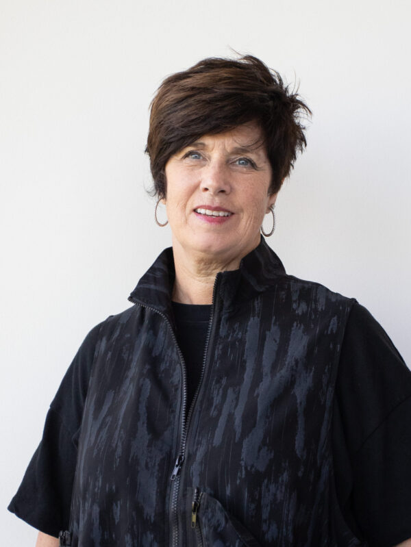 Portrait of a middle-aged woman with short dark hair wearing a black patterned jacket against a light wall.