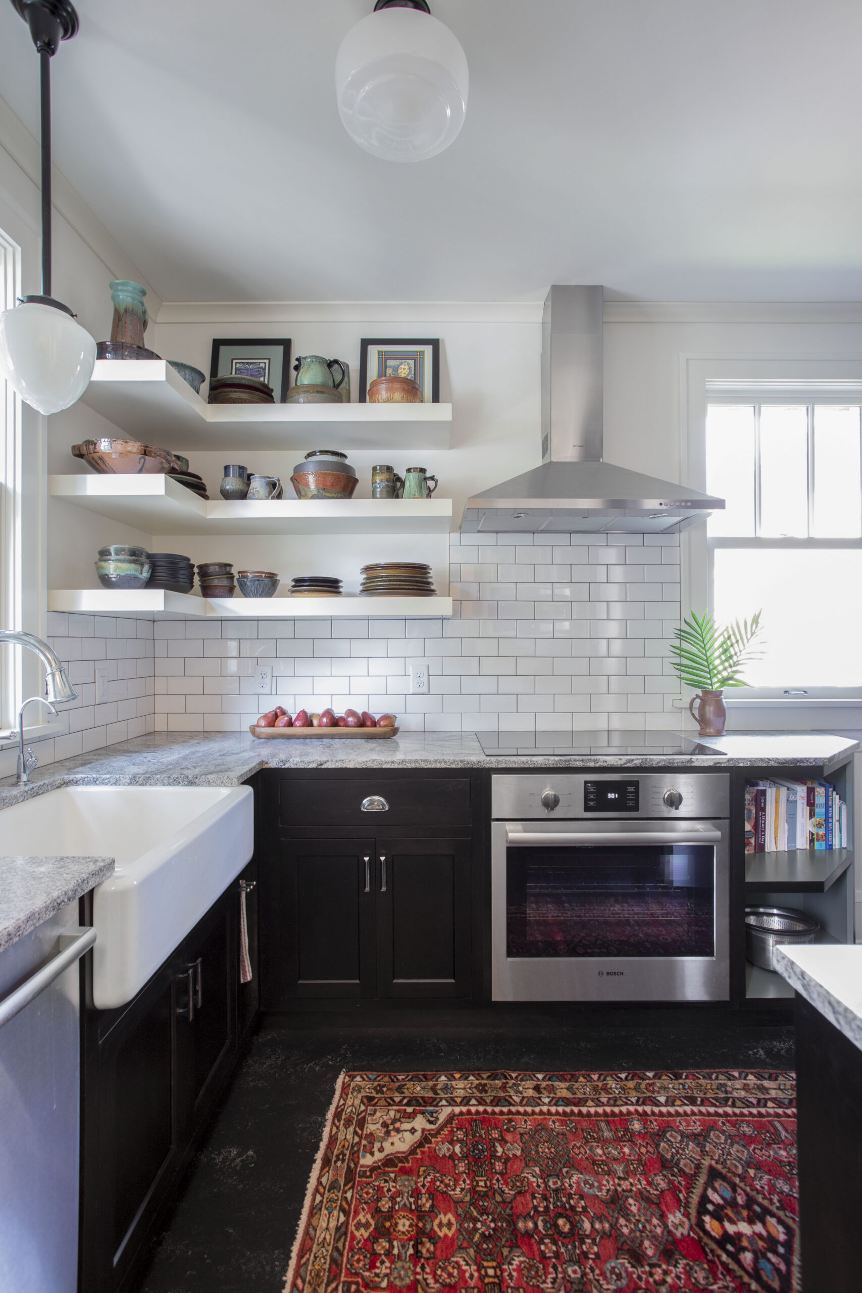 Kitchen with white open shelves holding pottery and framed art above a stainless range hood and white subway tile backsplash.