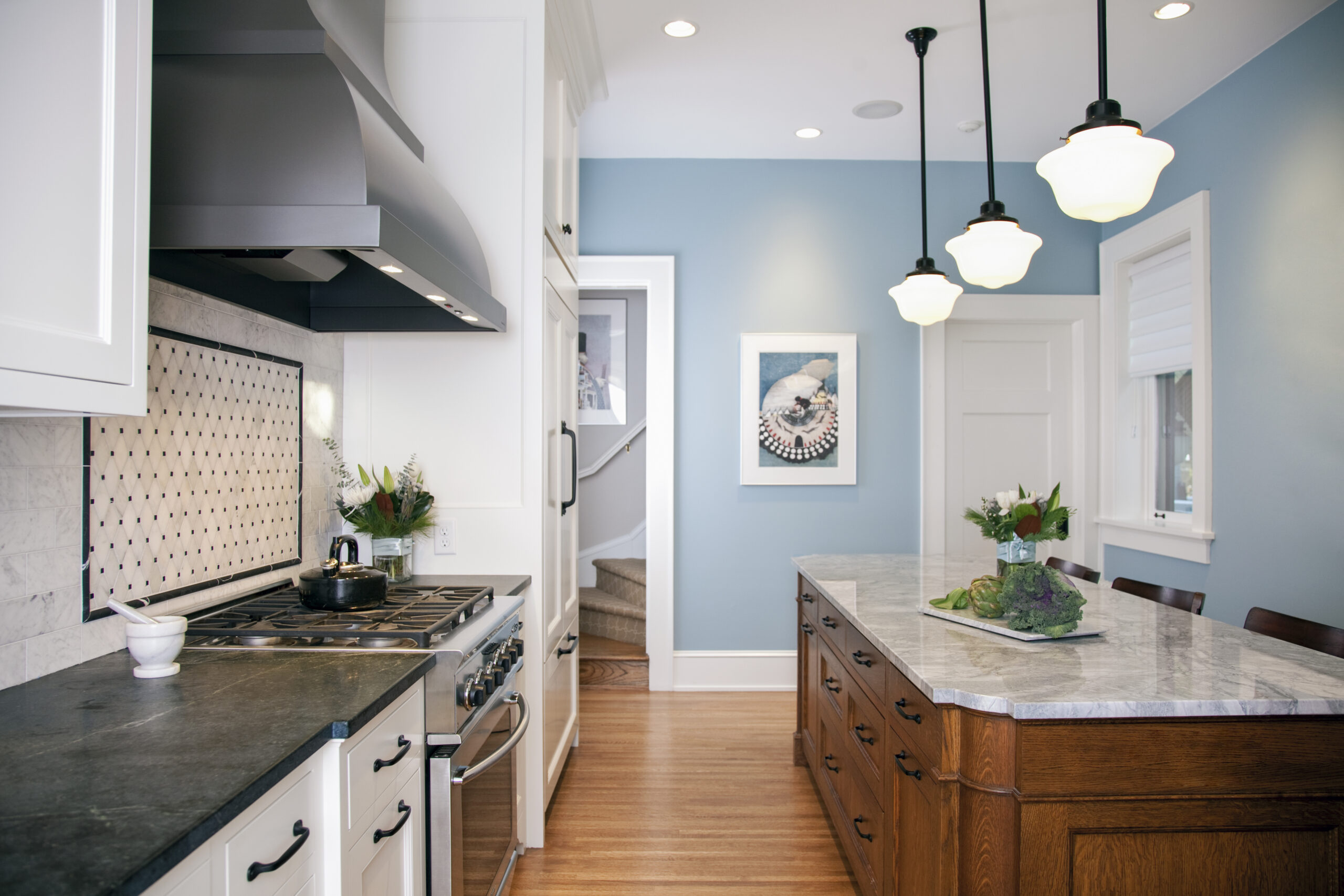 Modern kitchen with blue accent wall, white cabinetry, marble countertops, and pendant lighting designed by residential architects.