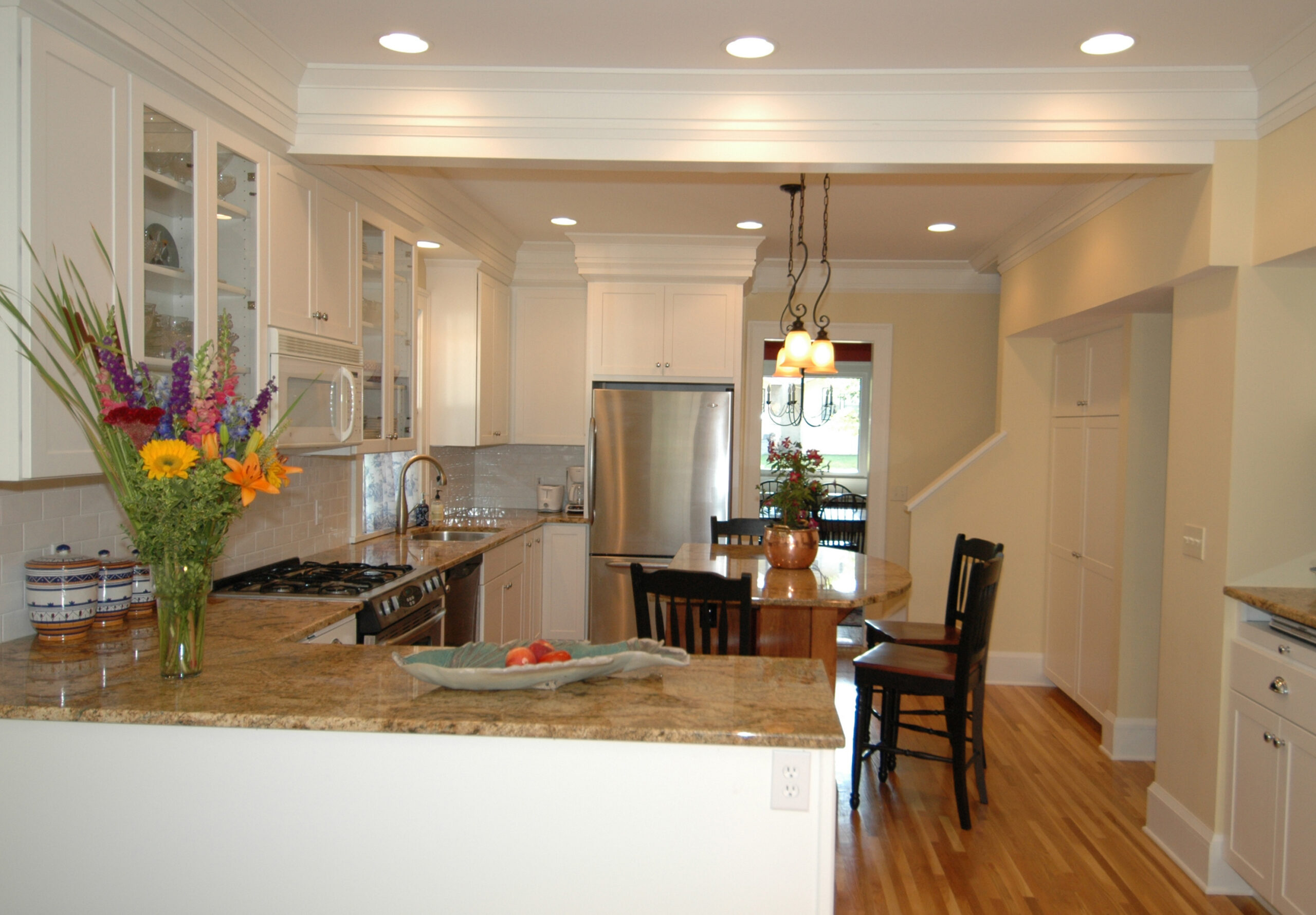 Bright kitchen with white cabinets, granite island, stainless-steel appliances, and a colorful flower arrangement on the counter.