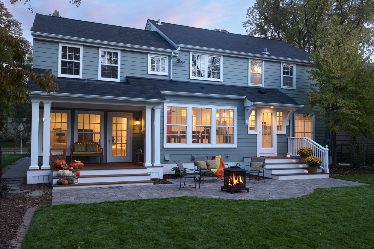Modern two-story home with blue siding, expansive patio, fire pit, and illuminated windows showcasing residential architecture design.