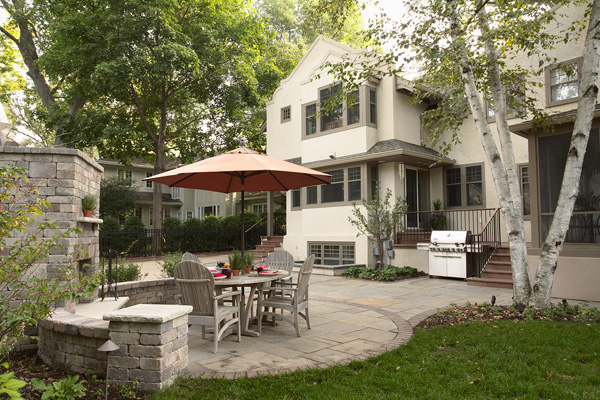 Modern white home with rear patio featuring dining area under umbrella and fireplace addition.