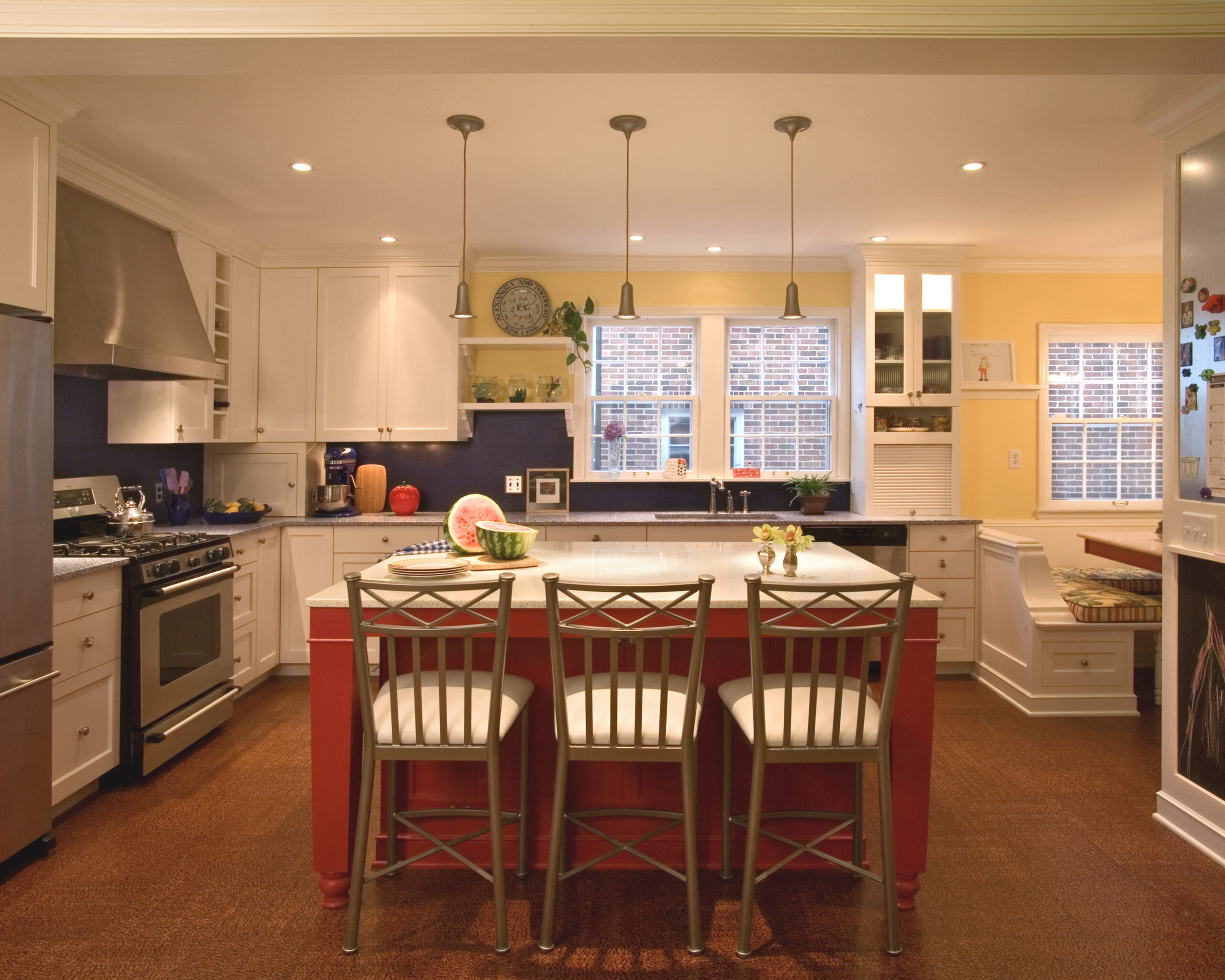 Bright kitchen with white cabinets, stainless stove, and a red island topped with fruit.