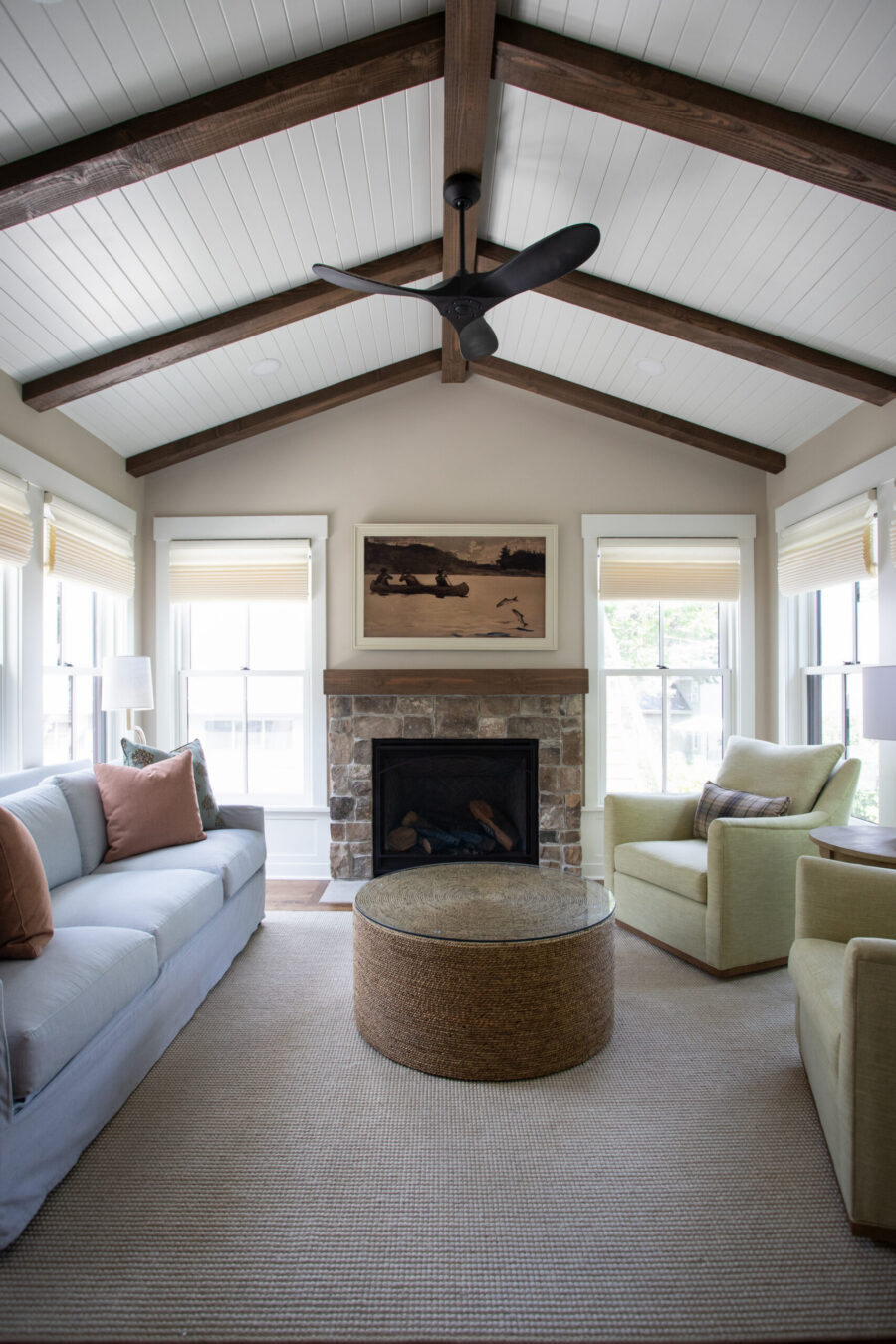 Cozy living room with a vaulted white paneled ceiling and dark wood beams, a black ceiling fan, and a stone fireplace.