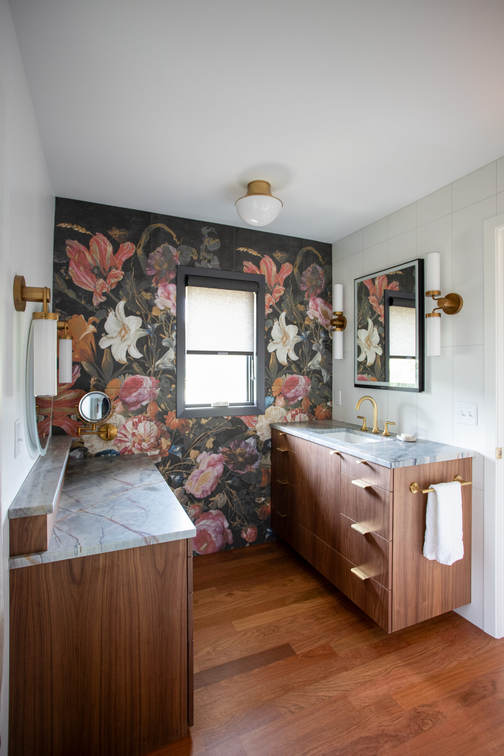 Bathroom vanity area with marble countertop, wooden cabinets, and brass fixtures against a dark floral wallpaper accent wall.