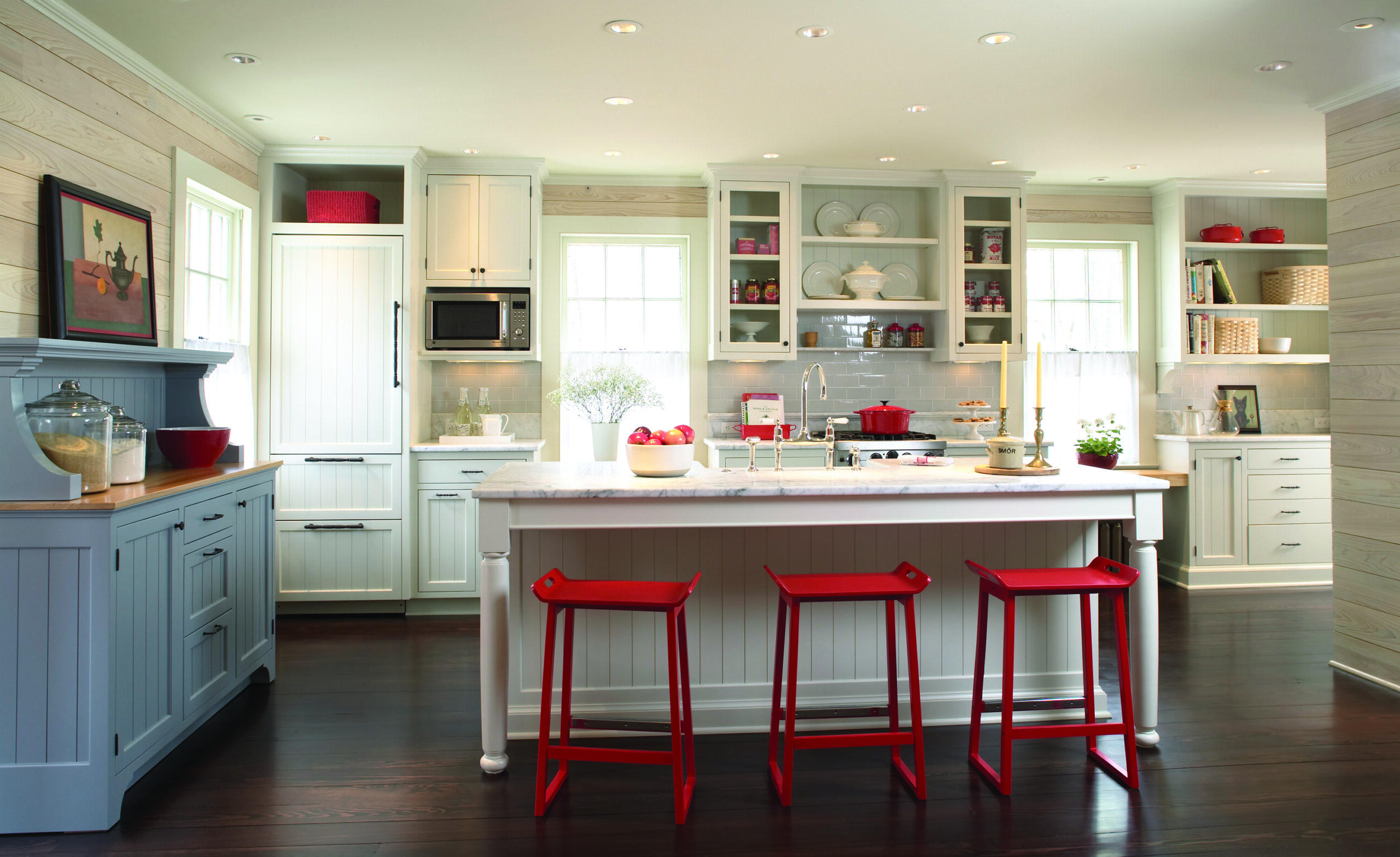 Bright white kitchen with an island and four red stools, open shelving, and a window behind the counter.
