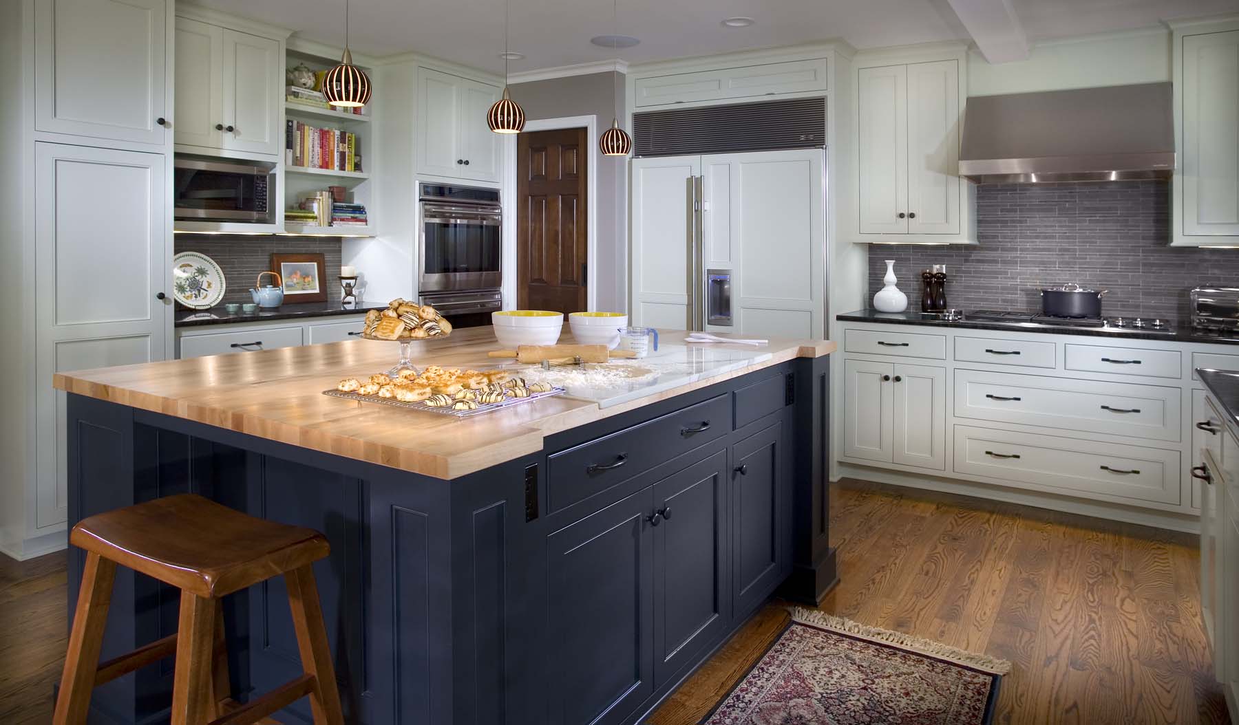 Modern kitchen with white cabinetry, dark blue island with wood countertop, pendant lights, and stainless steel appliances in a Minneapolis kitchen remodel.