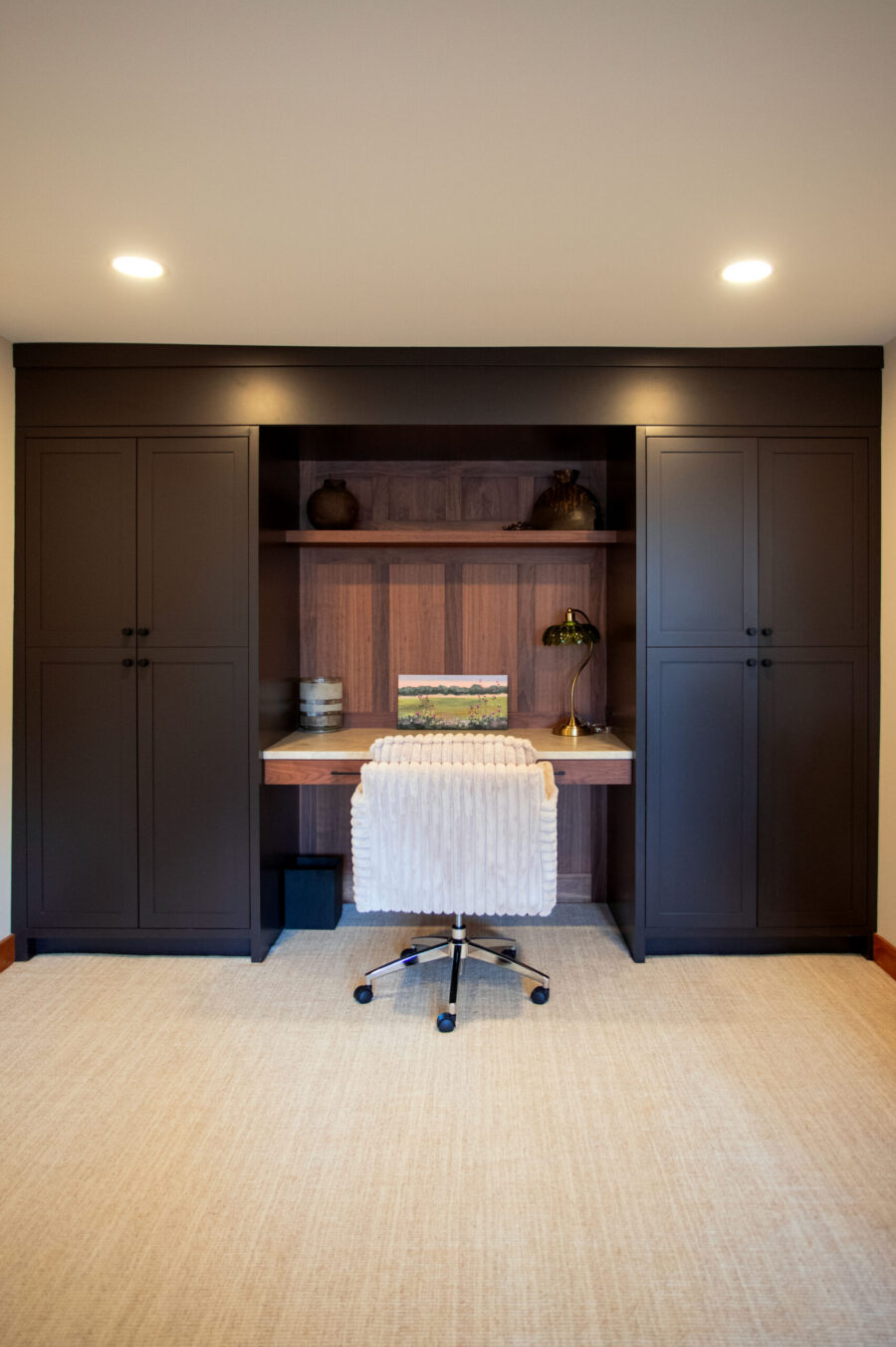 Dark brown built-in cabinet with an open shelf and a white office chair centered in a small workspace.