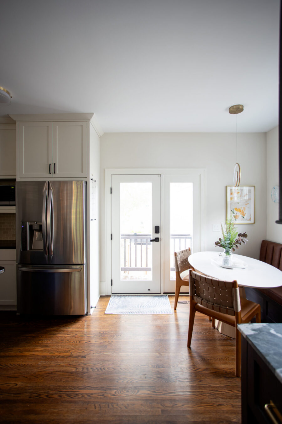 Bright modern kitchen with white cabinets and a stainless steel French-door refrigerator near a round white dining table by French doors.