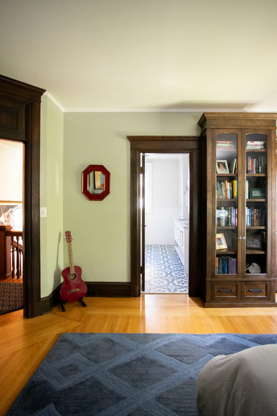 Green-walled living room with dark wood built-ins; a red acoustic guitar rests on the floor beside a red octagonal mirror.