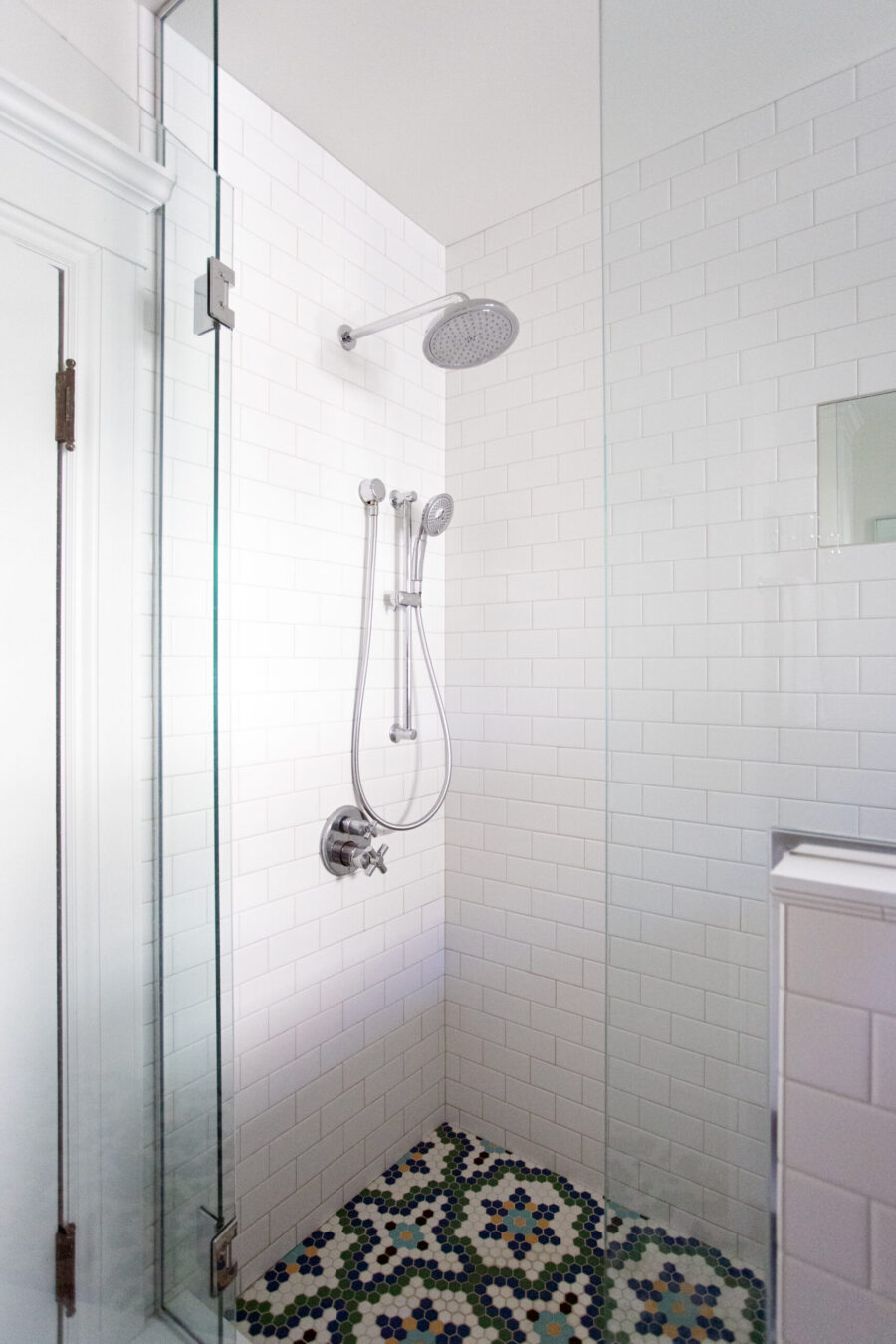 Glass-walled shower with white subway tile walls, a ceiling rain shower and a handheld shower, and a colorful hex mosaic floor.